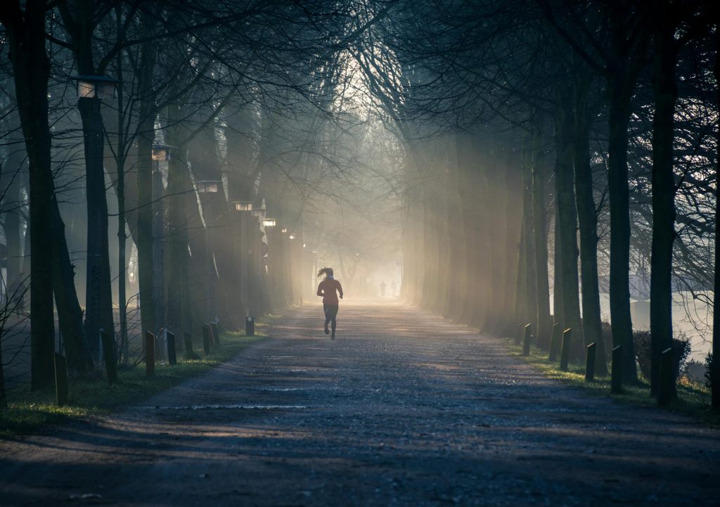 Une femme court dans un sentier entre les arbres le matin.